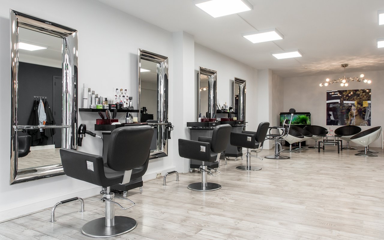 De salon van Kapsalon Cronjé: drie kappersstoelen voor grote spiegels met zilveren lijsten, witte muren en een lichte vloer