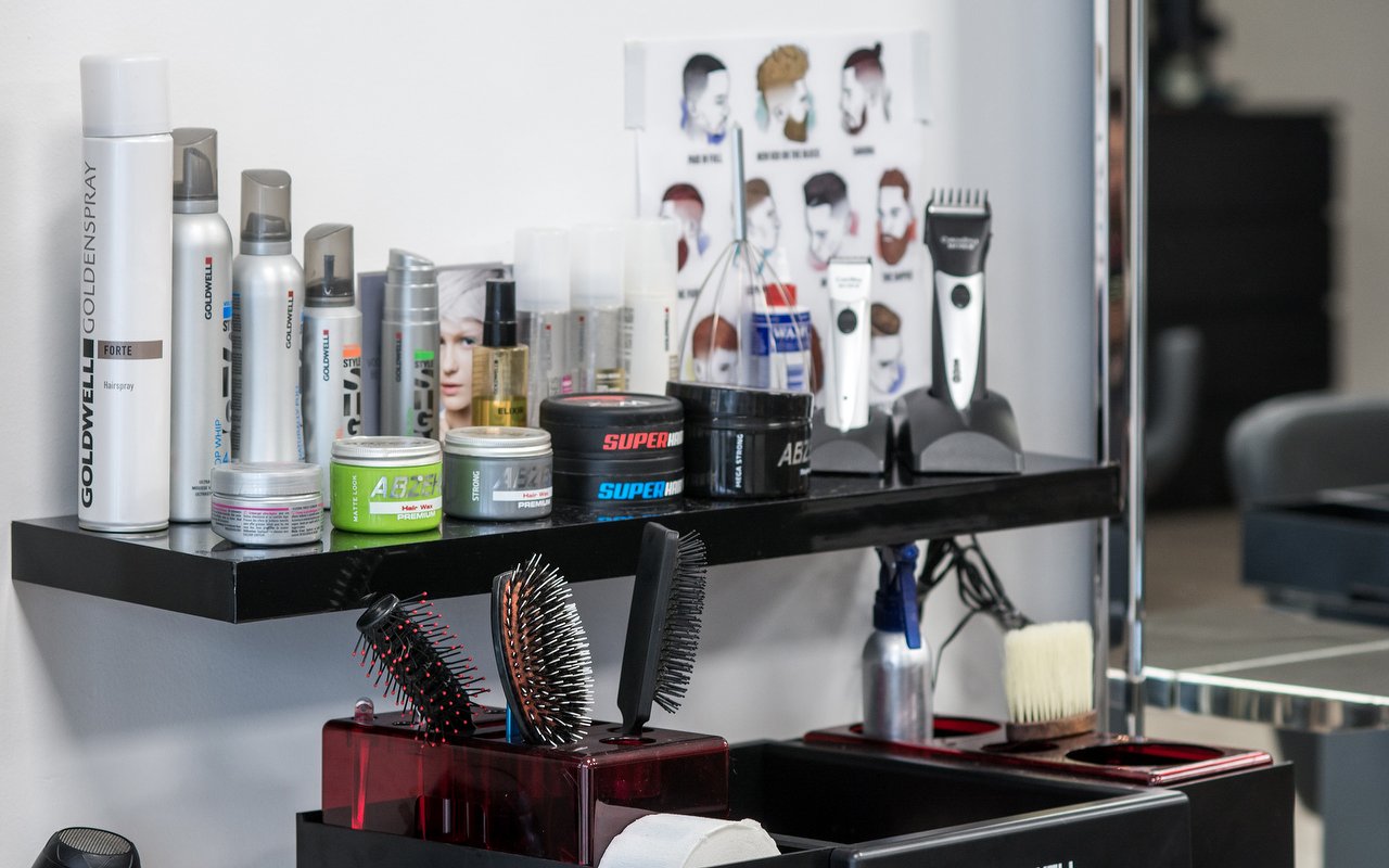 Een spiegelplank met Goldwell-stylingproducten, borstels en tondeuses, met een poster van herenkapsels op de achtergrond
