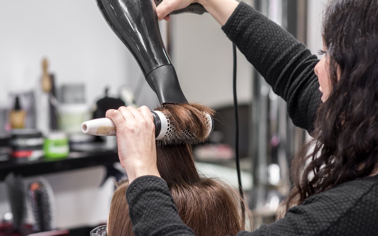 Een kapster föhnt lang bruin haar met een ronde borstel